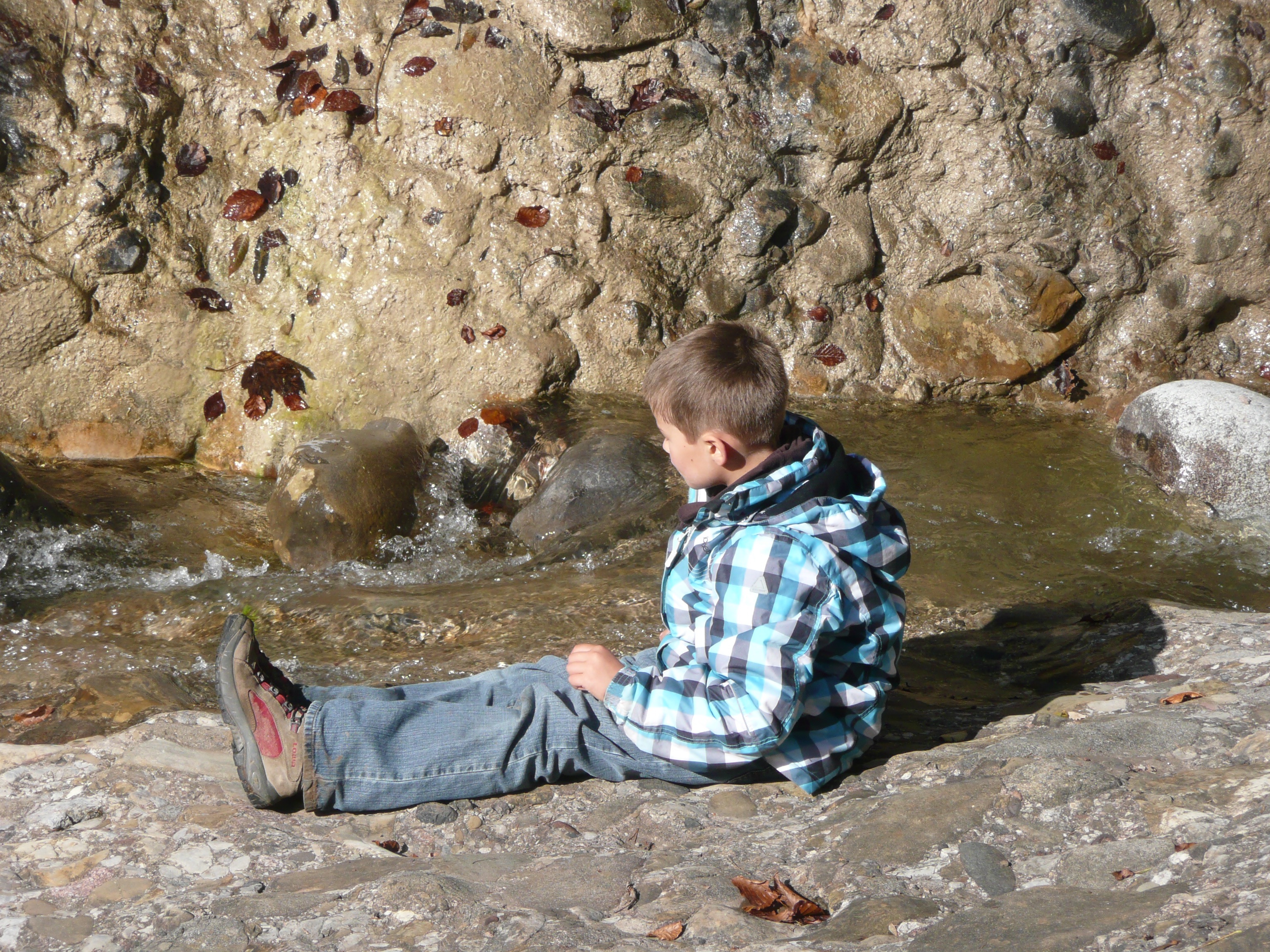 Ein Junge sitzt am Ufer eines Baches und blickt aufs Wasser. 