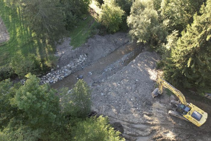 Lufaufnahme von einem Bagger am Bach, an dem gerade Bauarbeiten für eine Revitalisierung stattfinden.
